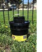 Black plastic containers stacked on grass against a chain-link fence.