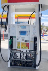 Gas pump at a station with visible internal components, including hoses and meters, under a white and yellow shelter.