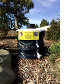 Yellow-and-black garden supply bag on mulch with caution sign and QR code, in daylight.