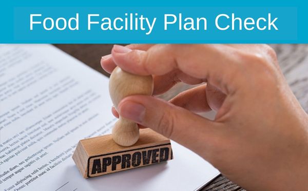 Hand stamping 'APPROVED' on a food facility plan document indicating a successful plan check.