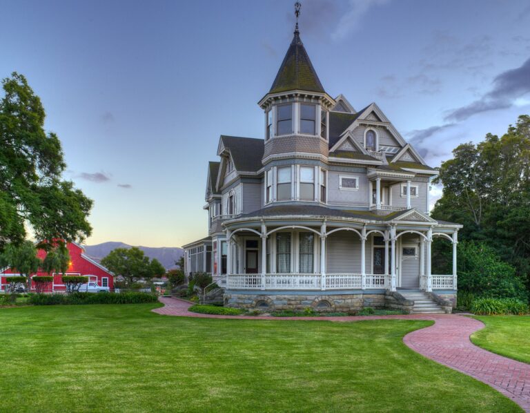 Victorian-style house with an ornate turret and wrap-around porch, set against a backdrop of a clear sky.