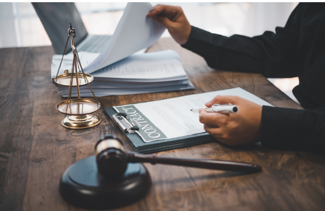 A person reviewing documents at a desk with a gavel, scales of justice, and a contract.