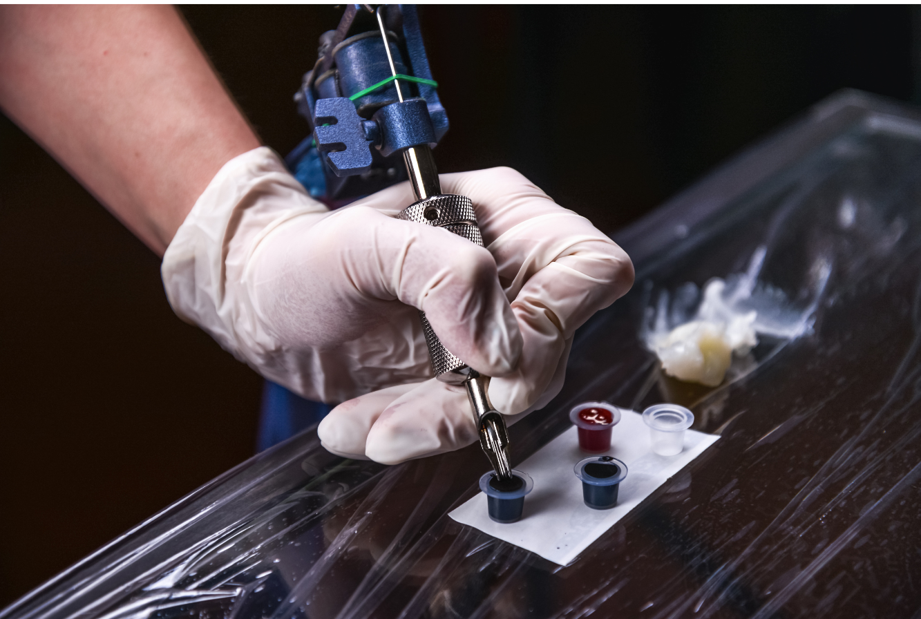 A person wearing gloves preparing a tattoo machine with ink.