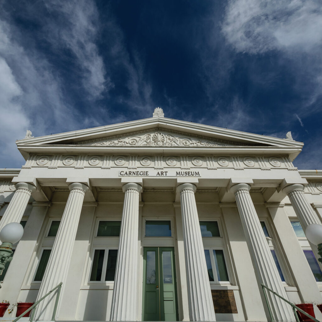 Looking up at the façade of the Carnegie Art Museum, featuring Doric columns and ornate architectural details.