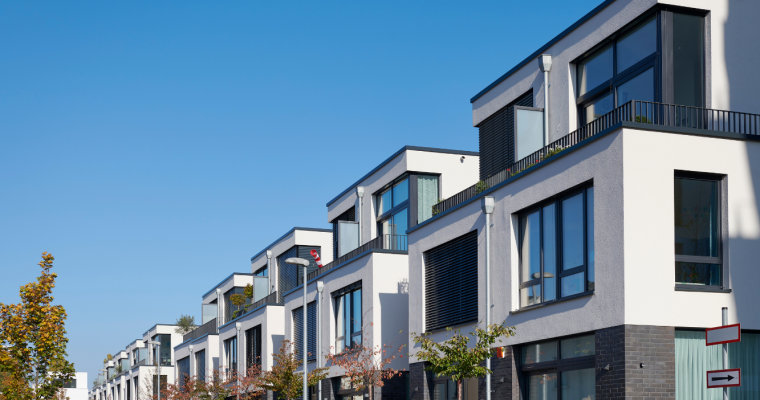 Row of modern townhouses with trees and blue sky in the background.