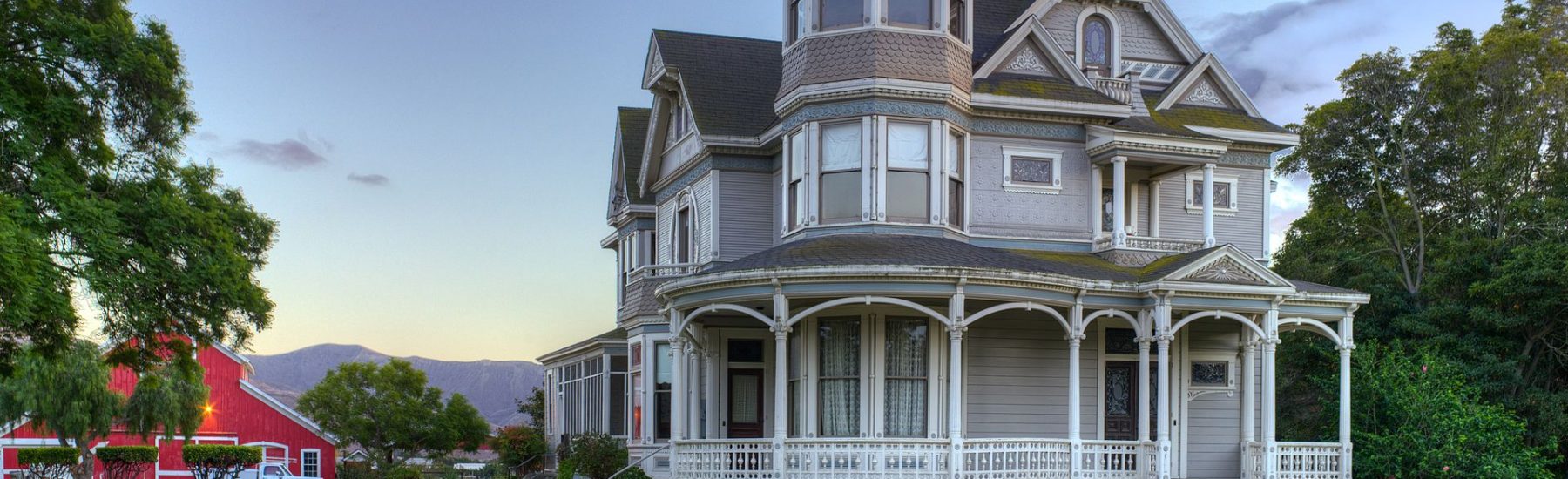 Victorian-style house with an ornate turret and wrap-around porch, set against a backdrop of a clear sky.