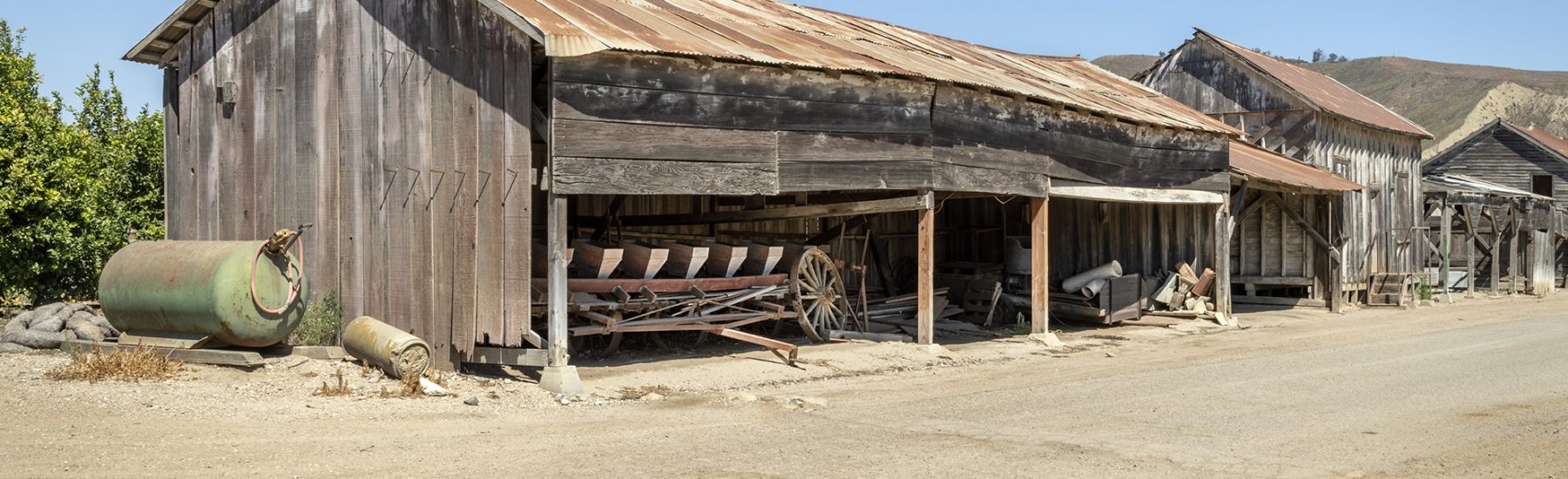 Rustic wooden buildings along a dusty street in a historical town with clear blue sky.