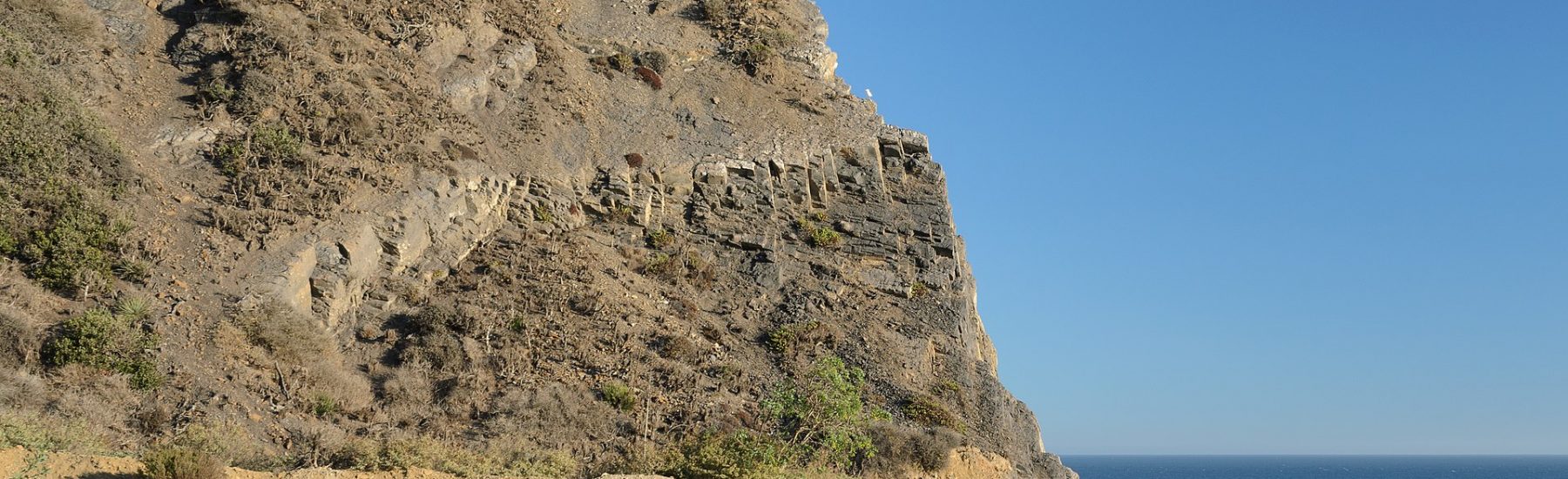 View of Mugu Rock at Point Mugu State Park, a coastal landmark with rugged terrain and the Pacific Ocean in the background.